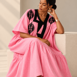 Seated model in the Ayo pink pinstripe embroidered linen bubu, showing its relaxed fit, wide sleeves and flowing hem
