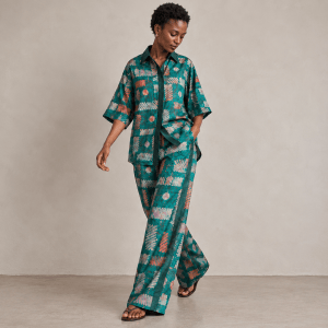 Model walking in Zuri teal Adire shirt and wide-leg trousers with contrasting Aso Oke side stripes.