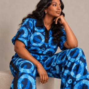 Model seated in the blue Zuri Polo Adire two-piece set, showing the polo neckline, rolled sleeves and extra-wide trousers.